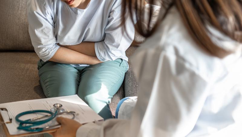 woman sits on couch holding abdomen