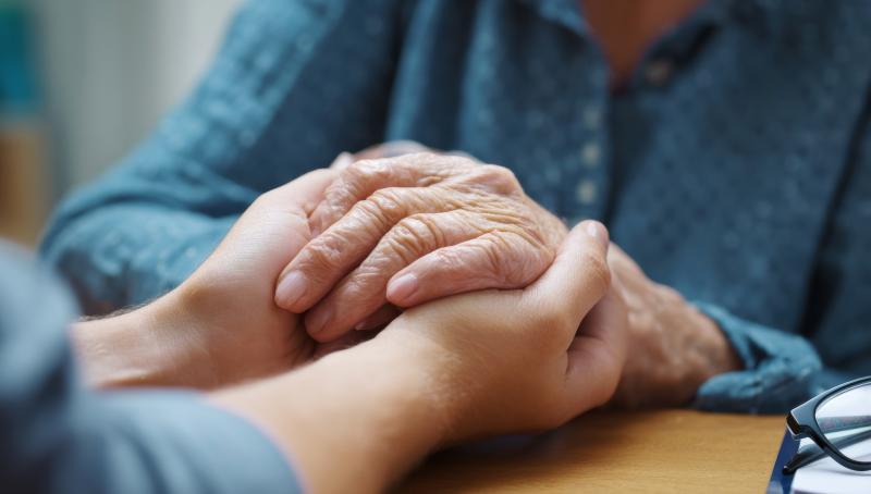A person gently holding the hands of an older adult across a table, conveying comfort and support.