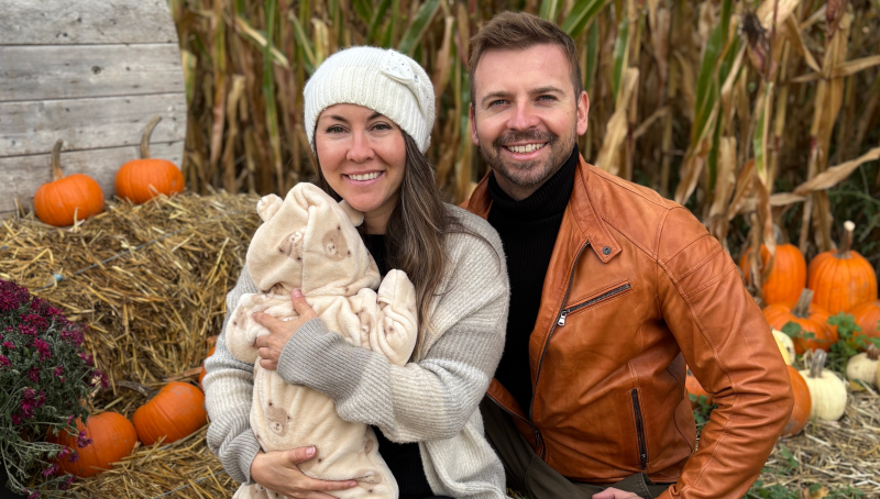 woman holding baby sits next to a man in against a fall backdrop