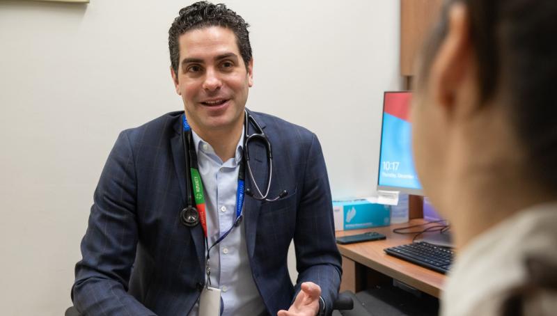 Dr. Nathan Stall, Geriatritician, Clinician Scientist and Geriatrics Site Lead at Sinai Health, sits with a patient in an exam room at Mount Sinai Hospital.