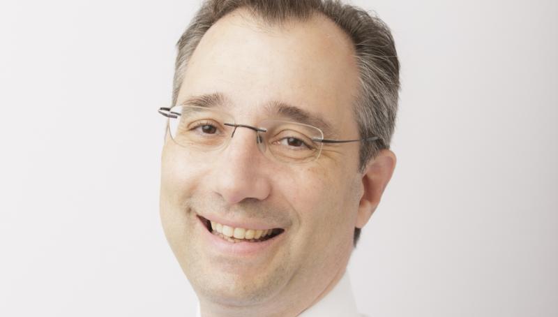 Dr. David Gratzer, head and shoulders portrait. He is looking at the camera smiling and wearing a white shirt with a blue tie