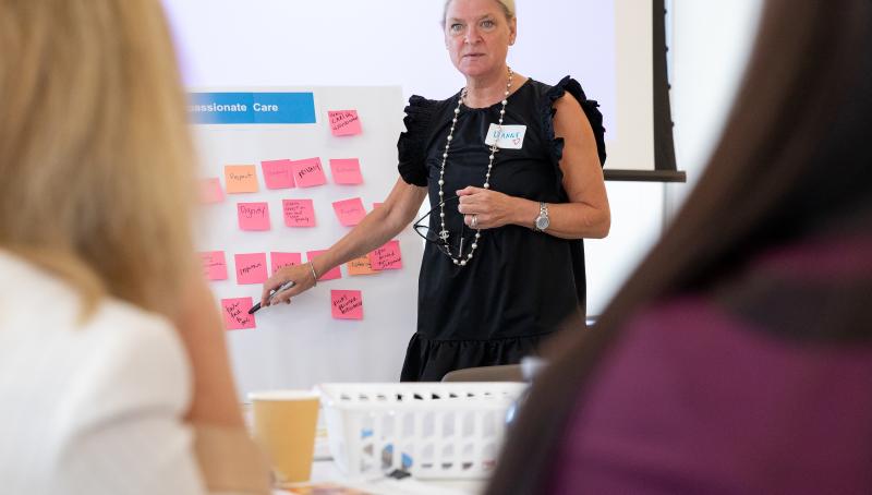 Dr. Lianne Jeffs pointing to a whiteboard with compassionate care descriptors during a presentation. 