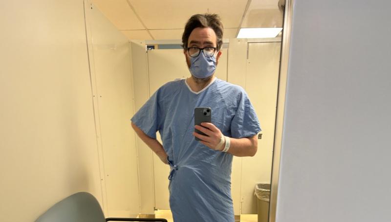 Man wearing hospital gown stands in bathroom