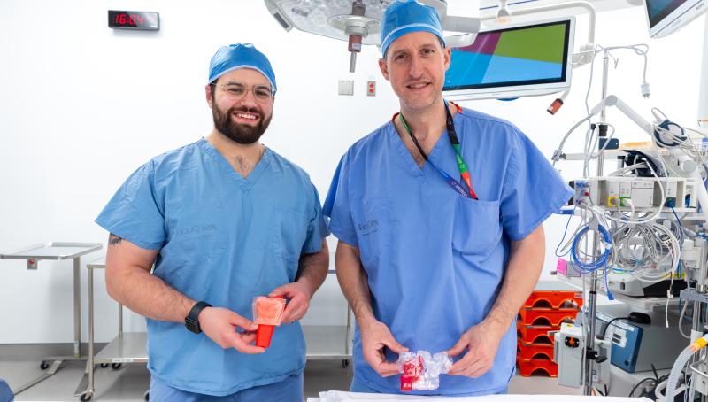 Qwynn  Ferreira and Dr. Joel Davies smiling and standing in an operating room holding the 3D models used in surgery.