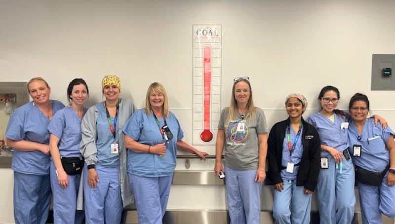A group of staff members from the Peri-operative services team smile beside a poster showing their recycling goals have been met.