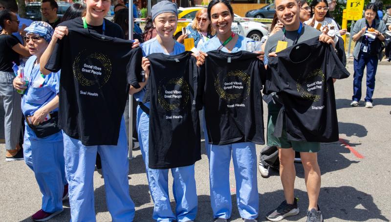 Four Sinai Health employees stand outdoors at the People Appreciation BBQ, smiling and holding black “Good Vibes Great People” T-shirts.