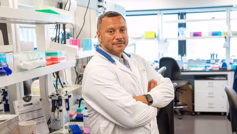 Dr. George Charames in a white lab coat standing in a laboratory.