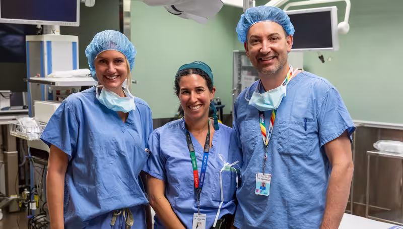 Three people standing in an operating room smiling.