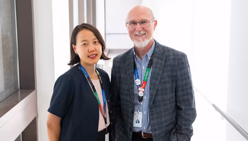 Two people in a brightly lit hallway standing beside each other smiling.