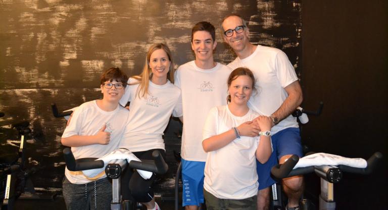 Man and woman sit on exercise bikes. Three children stand beside them. 