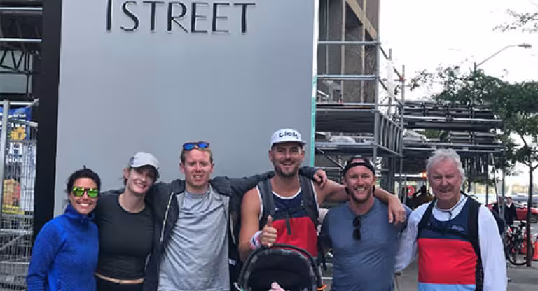 Six people, one holding a baby in a car seat, stand in front of a building that says 'one yonge street' on the side