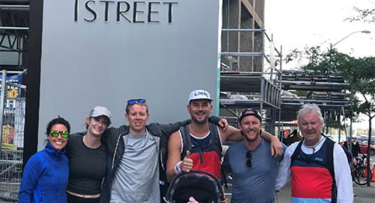 Six people, one holding a baby in a car seat, stand in front of a building that says 'one yonge street' on the side