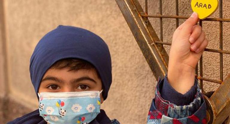 A child wearing a coat and a medical mask holds a heart-shaped lock