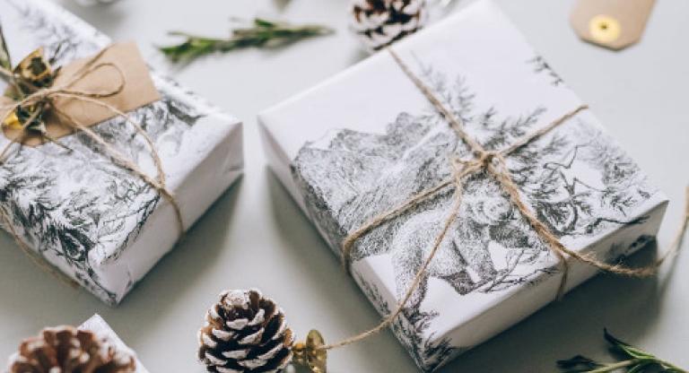 Holiday gifts wrapped in white paper and twine, surrounded by pinecones and greenery.