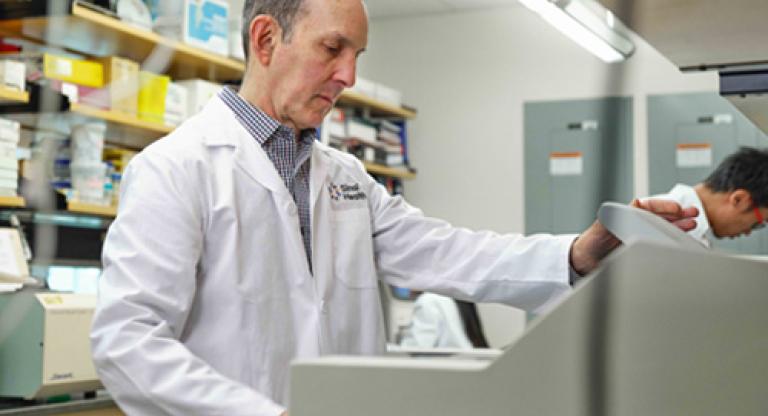 Man in white lab coat stands in front of medical equipment