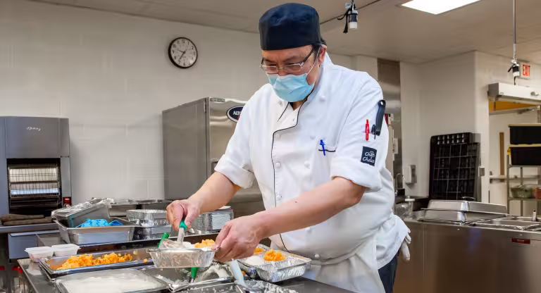 A man in a chef uniform preparing meals in a large industrial kitchen