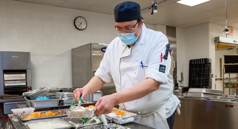A man in a chef uniform preparing meals in a large industrial kitchen