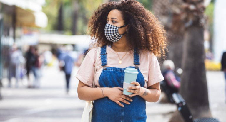 Pregnant woman is wearing a mask and holding coffee