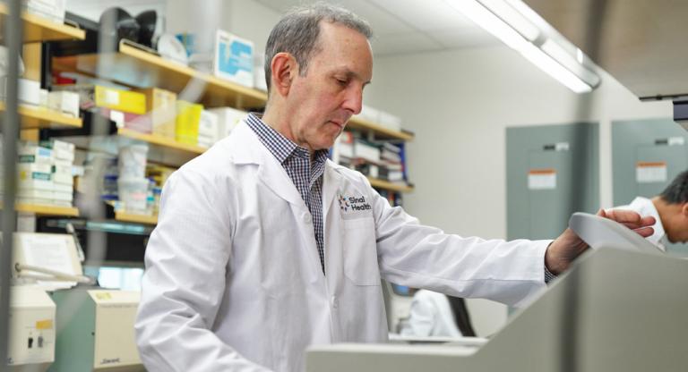 Dr. Daniel Drucker operating a lab instrument. He is wearing a white lab coat