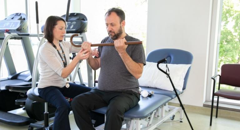 Physician helping man lift cane with both hands at rehabilitation centre.