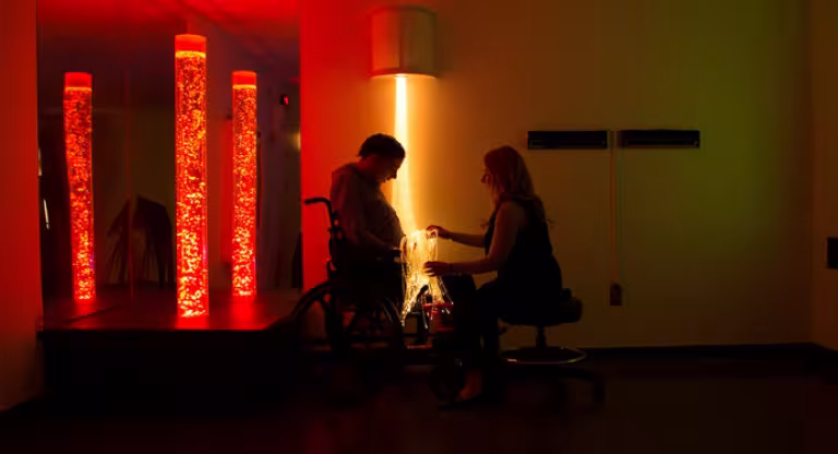 Woman sitting with person in wheelchair in dimly lit room with lights.