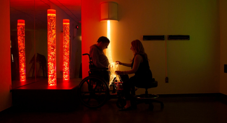 Woman sitting with person in wheelchair in dimly lit room with lights.