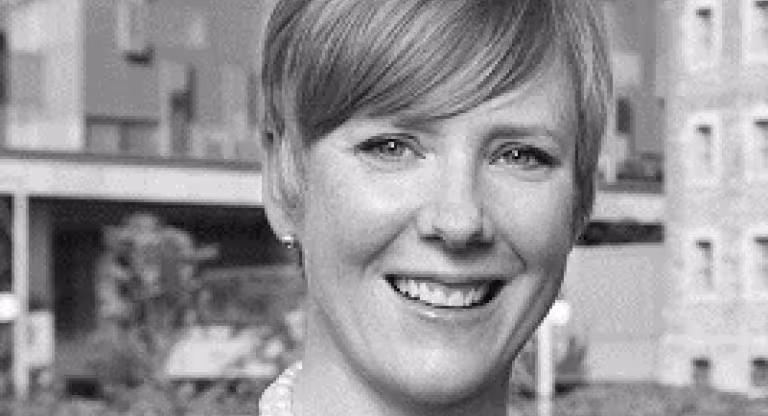 A headshot of a woman with a hospital in background