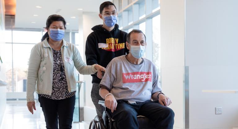 An older male in a wheelchair accompanied by his son and wife