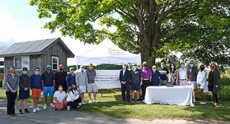 Group of people stand outside, next to a table with a trophy. 