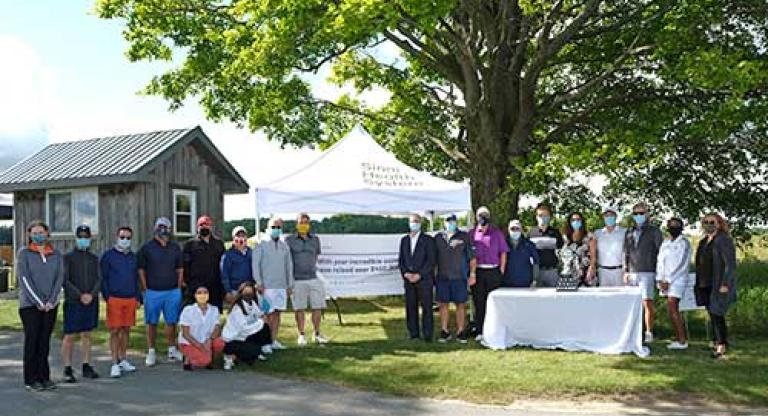 Group of people stand outside, next to a table with a trophy. 