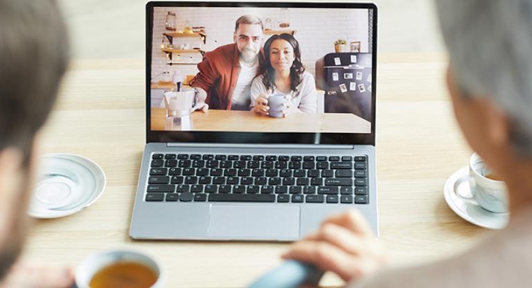 Two people using a laptop for a video chat with two other people. 