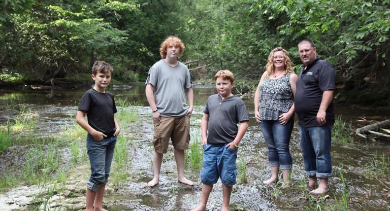 The Tummers family standing together in shallow river.