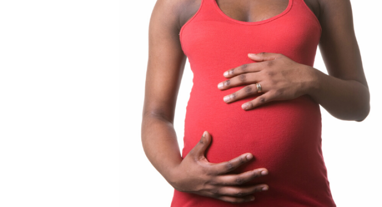 Pregnant woman in red shirt holding belly.