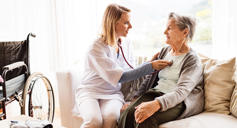 Woman listening to elderly woman's heart with stethoscope. 