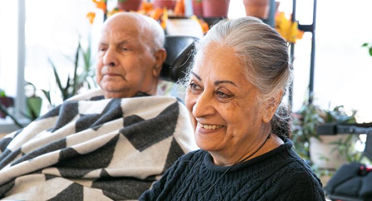 Female caregiver sitting beside elderly male, wrapped in a blanket