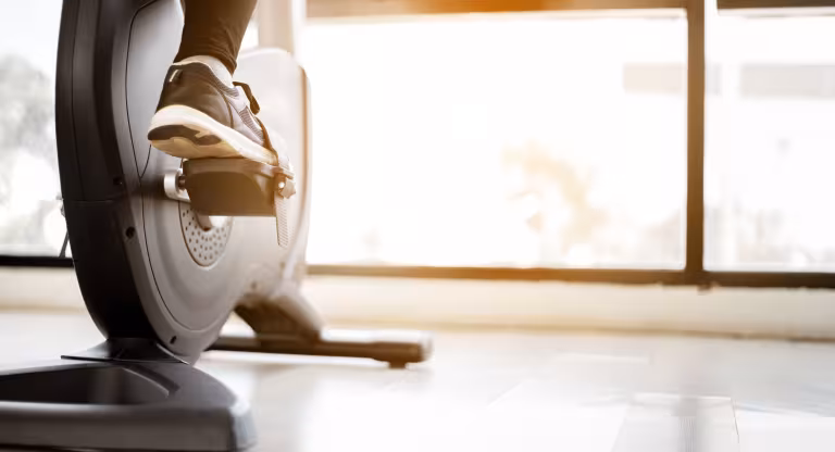 The foot of a person in running shoes riding a stationary bike indoors