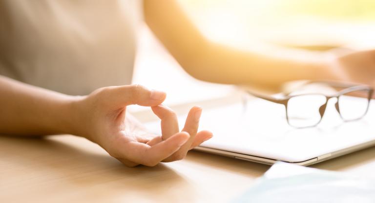 The hands of a person sitting at a desk meditating in front of a closed laptop