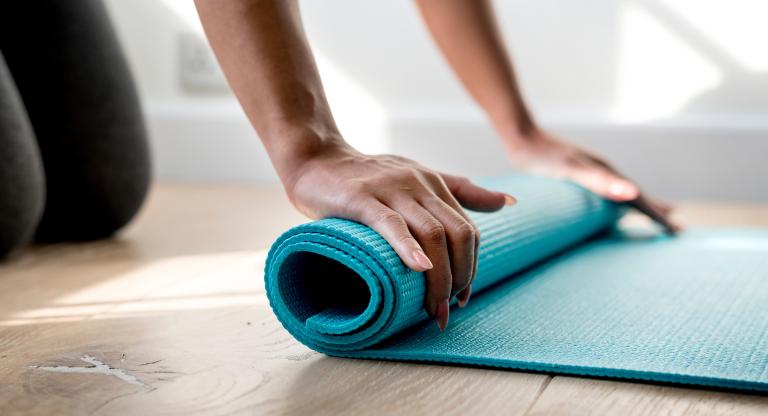 The hands of a person rolling up a blue yoga mat