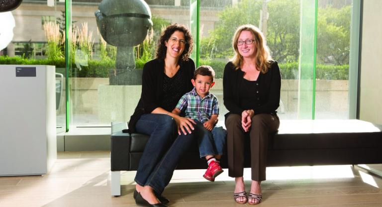 Two women sit with a young boy on a bench.