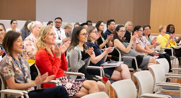 A group of people sits in an auditorium and applauds.
