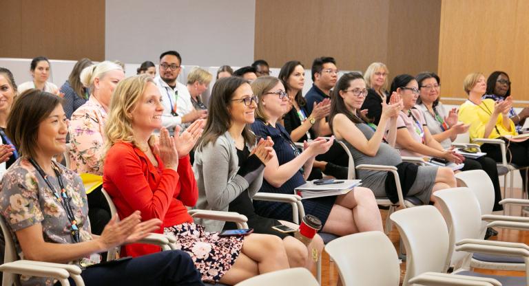A group of people sits in an auditorium and applauds.