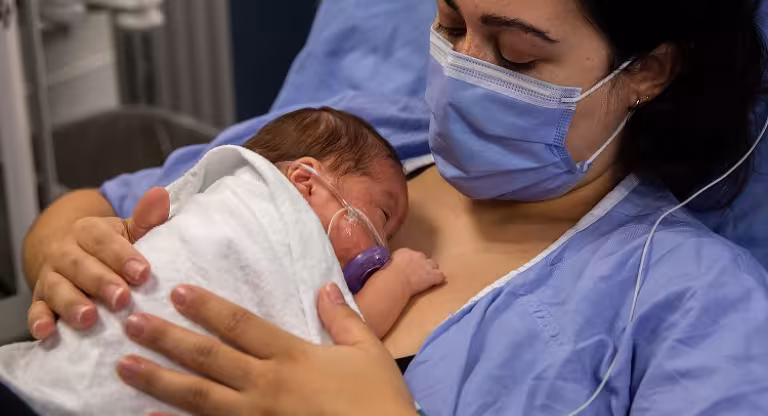 Woman wearing mask holds newborn on her chest