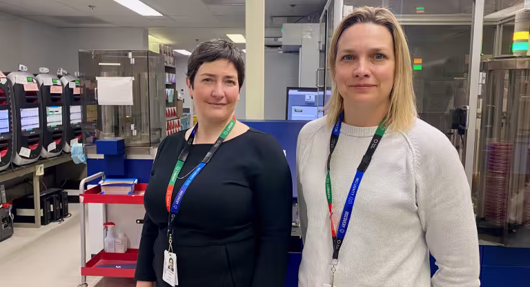 A phone of Dr. Anne-Claude Gingras beside Dr. Jennie Johnstone in the lab. 