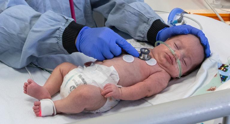 Nurse examining preterm baby with a stethoscope.
