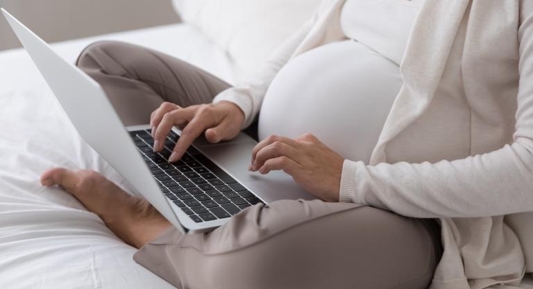 Pregnant woman using a laptop on her lap.