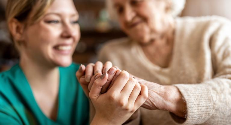 Close-up of a health care worker gently holding the hands of an older adult patient.