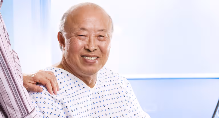 Senior Asian man with hand of caregiver on shoulder.