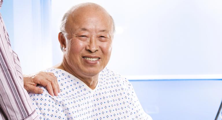 Senior Asian man with hand of caregiver on shoulder.