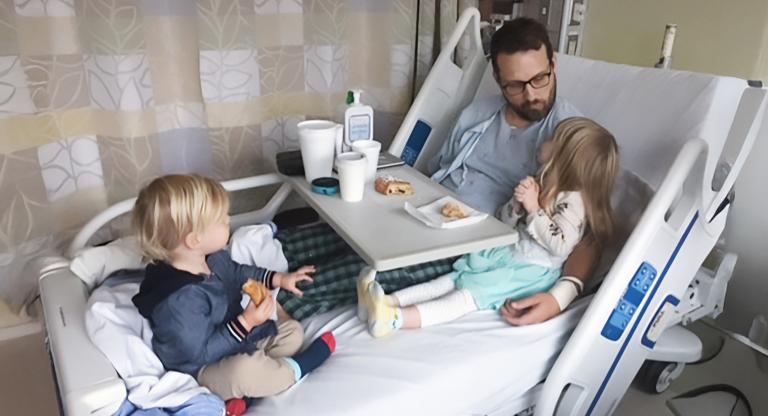 man sits in hospital bed with two young children