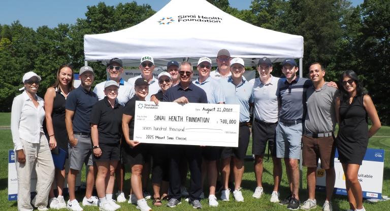 group stands outside holding presentation cheque
